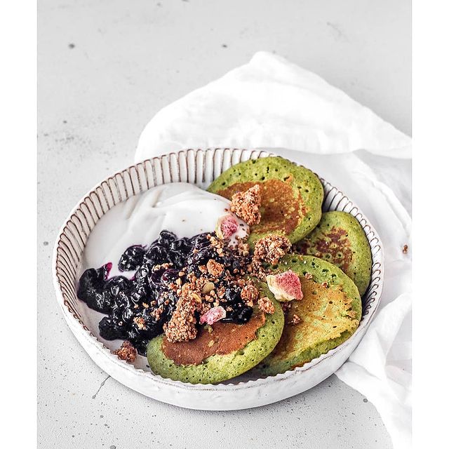 Green pancakes with fruit and a granola crumble on a white plate